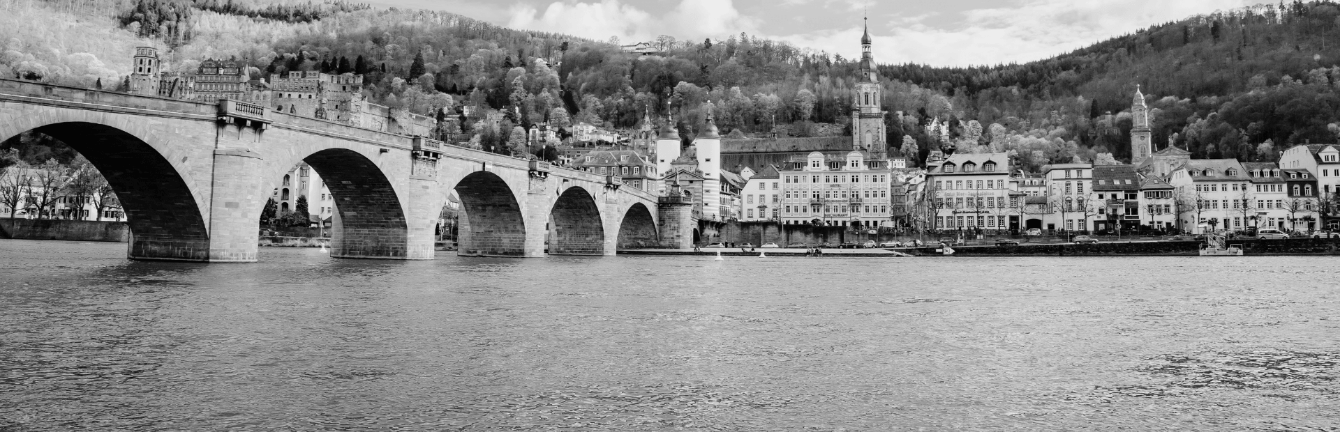 Die Alte Brücke in Heidelberg über den Neckar mit Blick auf die historische Altstadt und die bewaldeten Hügel der Region.