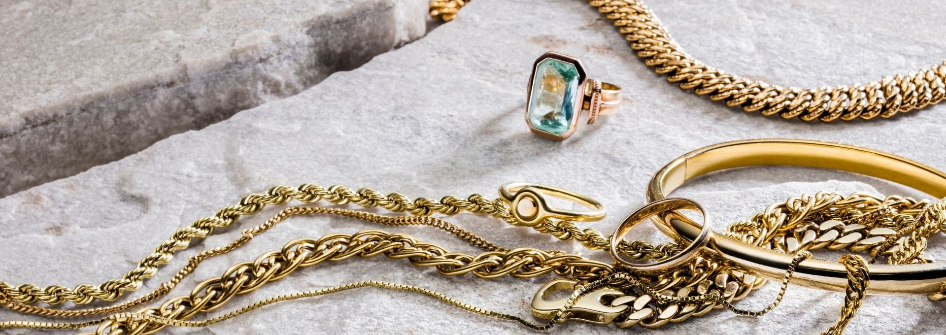 Verschiedene Altgold-Positionen wie Goldketten, Goldringe, Armreifen und Schmuckstücke aus Gold auf Naturstein. Die Darstellung veranschaulicht den Altgoldankauf sowie den Verkauf von Altgold und Goldschmuck in den Filialen der Rheinischen Scheidestätte.