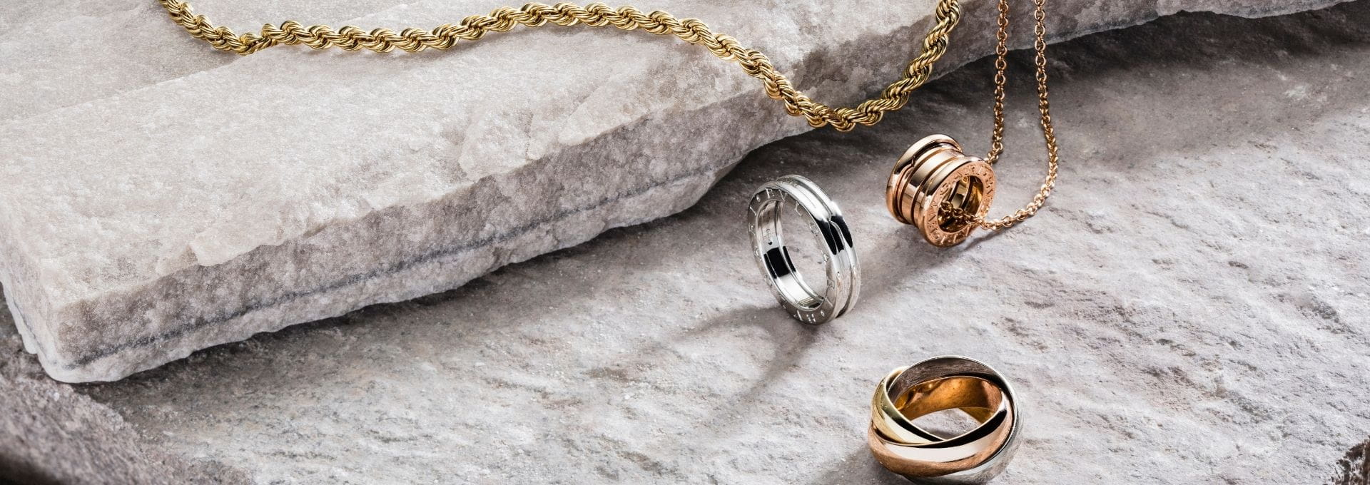 Goldene Halsketten, Ringe und Anhänger aus Weiß-, Gelb- und Roségold auf heller Steinoberfläche für Schmuckankauf und Schmuckverkauf.