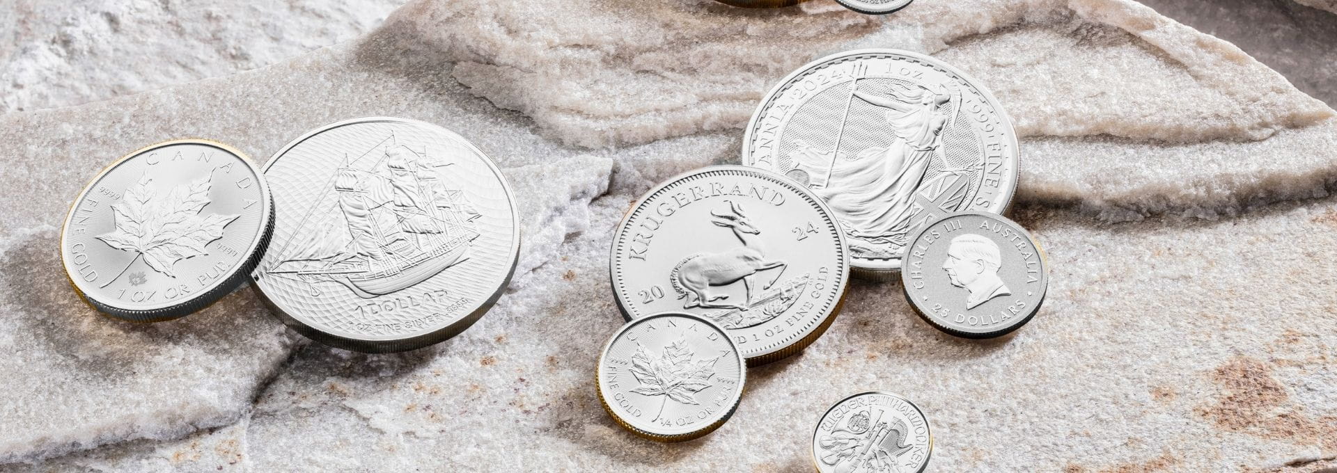 Hochwertige Silbermünzen mit bekannten Anlagemotiven auf Naturstein. Die Darstellung veranschaulicht den Kauf von Silber in Form von Anlagemünzen und zeigt beliebte Silbermünzen für die langfristige Vermögenssicherung.