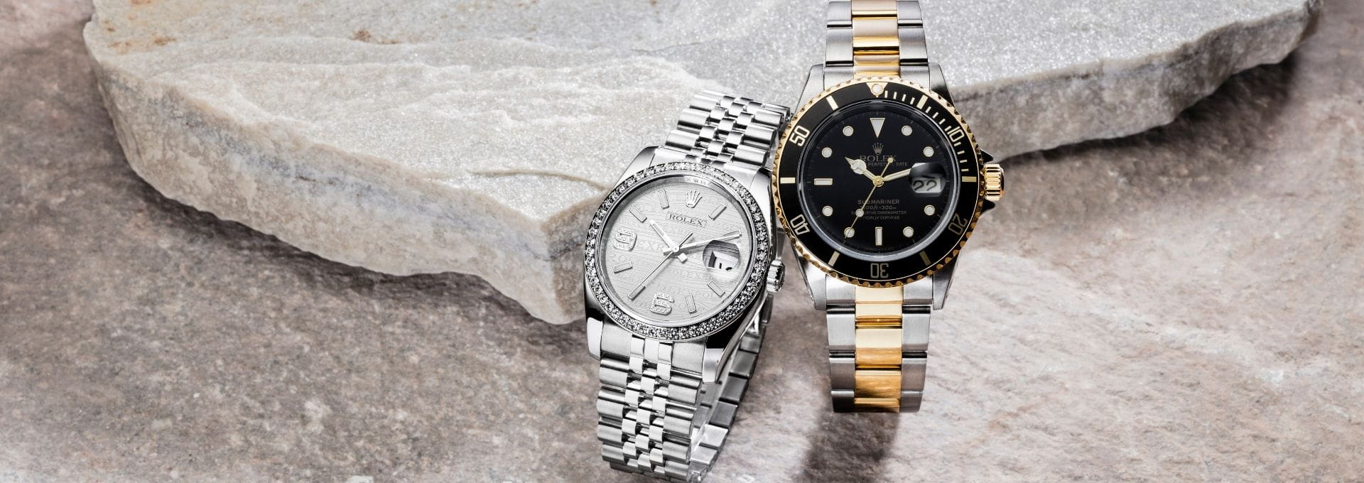 Zwei luxuriöse Armbanduhren aus Edelstahl und Gold auf heller Steinoberfläche als Symbol für professionellen Uhrenankauf hochwertiger Markenuhren.